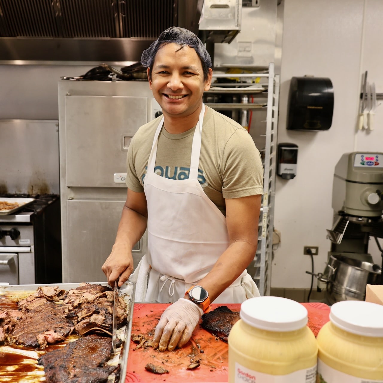 Avishar smiles at the camera while cutting up meat for meals