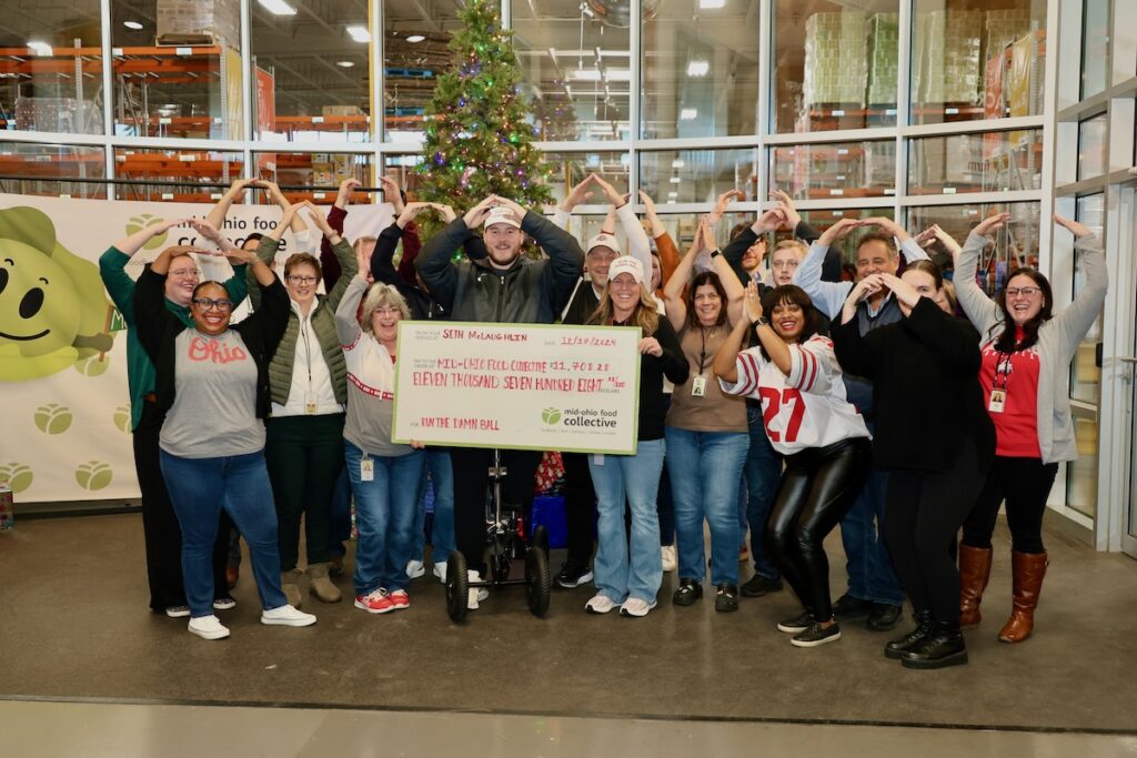 Seth Mclaughlin stands with MOFC employees presenting his check. They all hold their hands over their head, making the O symbol for Ohio