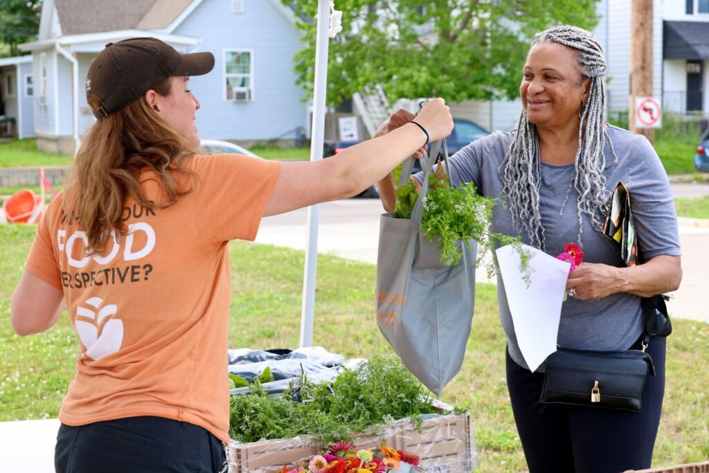 Mid-Ohio Farm Senior Project Manager Audrey Beam hands a bag of herbs to smiling neighbor Ingrid Dunson