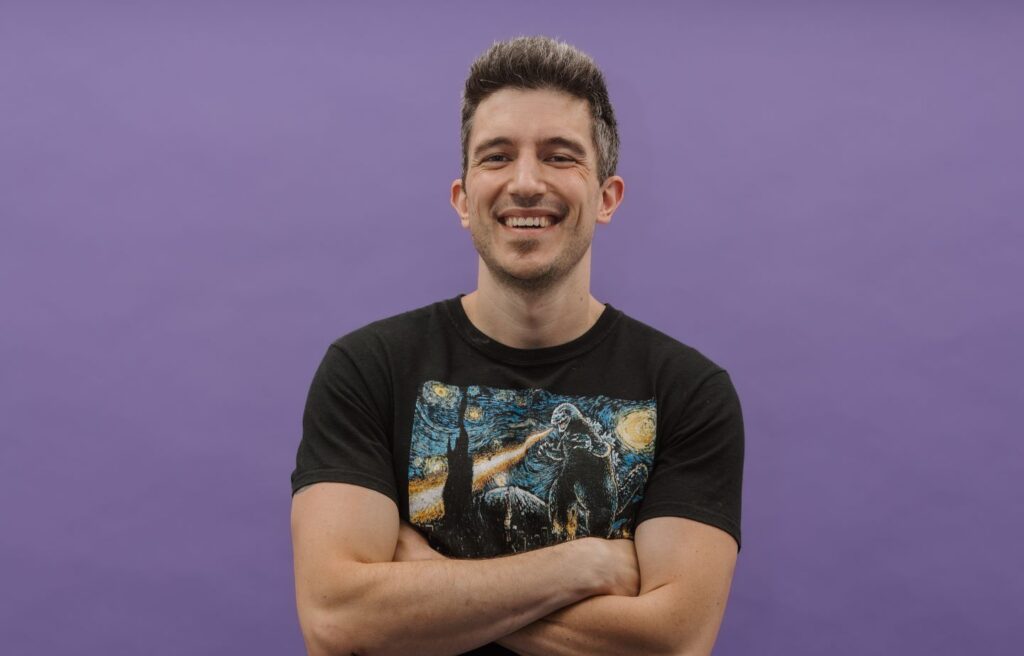 Man smiles with arms crossed against a purple background